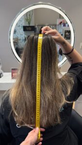 Medición del largo total del cabello con cinta métrica en un salón de peluquería